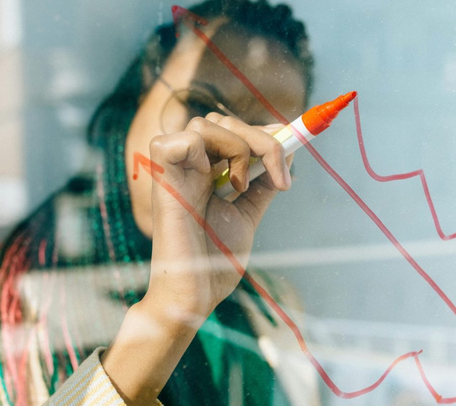 A businesswoman draws a red financial graph on a glass panel, symbolizing strategy and success.