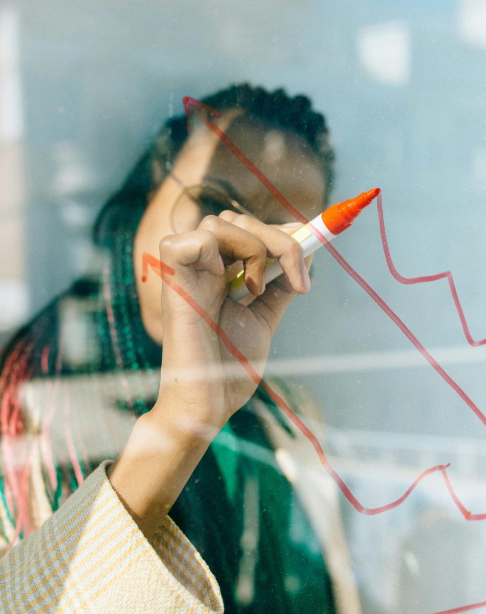 A businesswoman draws a red financial graph on a glass panel, symbolizing strategy and success.